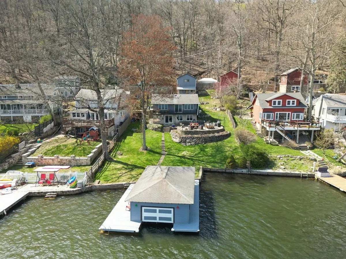 Aerial view of 213 Hudson Avenue, Hopatcong NJ — a blue lakefront home with terraced lawn and a private gray boathouse on a dock at the edge of Lake Hopatcong. Listed by BB Angjushev at Sotheby's International Realty.