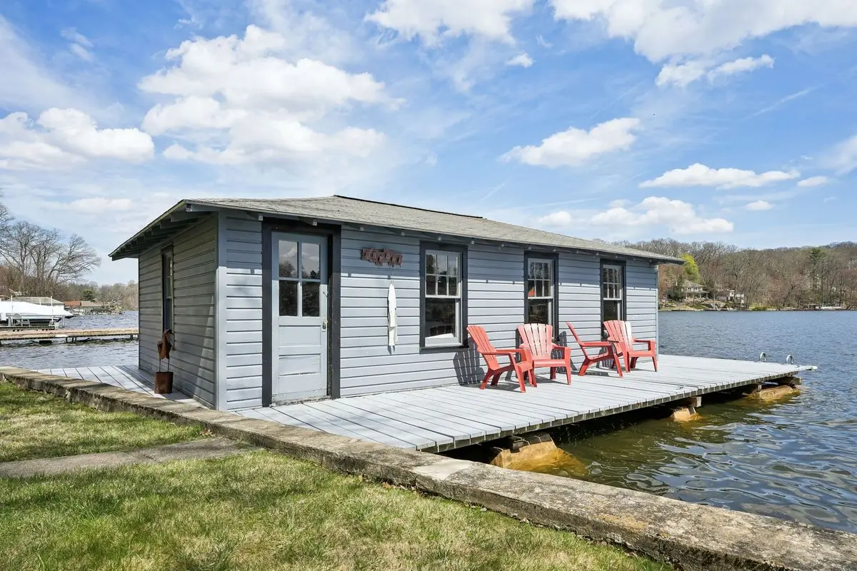Private gray boathouse and sundeck with red Adirondack chairs on the dock, set directly on the water of Lake Hopatcong at 213 Hudson Avenue