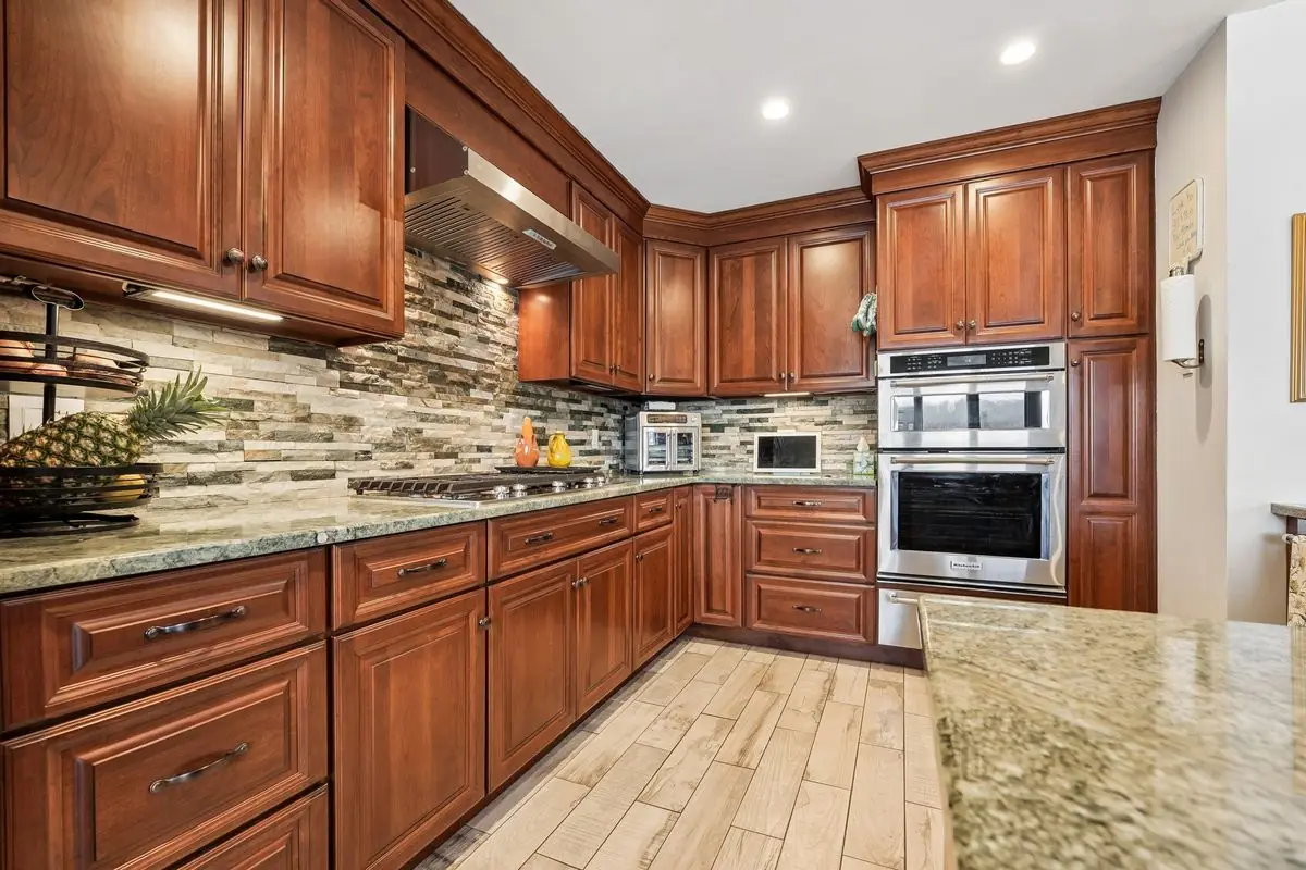 Updated kitchen with cherry wood cabinetry, granite countertops, stacked-stone backsplash, stainless double wall oven, and gas cooktop in the Hopatcong lakefront home