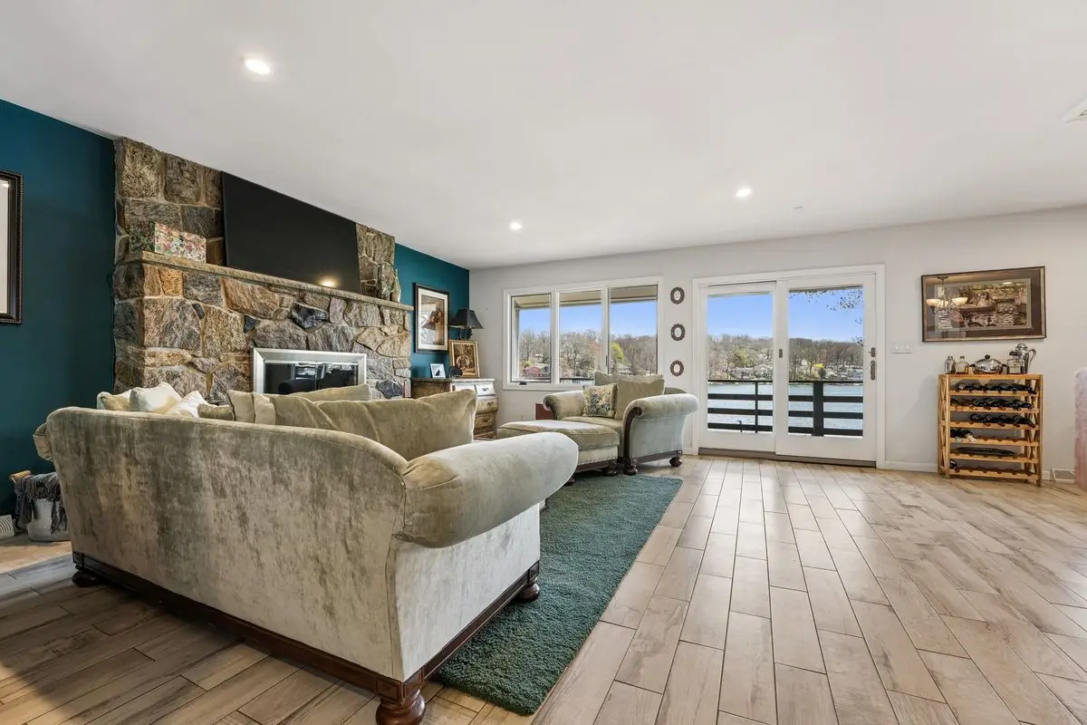 Living room with floor-to-ceiling stone fireplace, teal accent wall, wood-look tile floors, and sliding glass doors opening to a lake-view deck at 213 Hudson Avenue