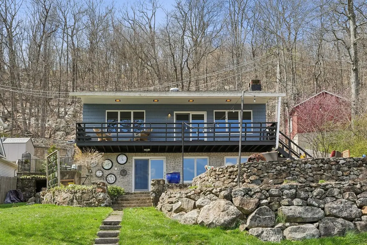 Lake-facing rear facade of the blue 213 Hudson Avenue home, with an elevated entertaining deck above a stone-walled terrace and landscaped lawn