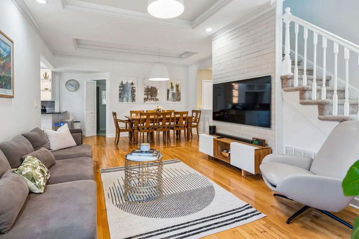 Bright open living and dining area with a white-plank custom media wall, tray ceiling with crown molding, hardwood floors, and a farmhouse dining table at 26 Oak Street