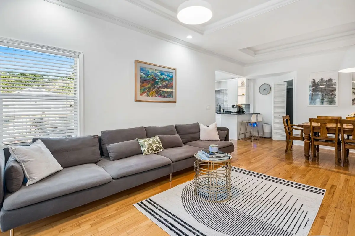 Living room with a gray sectional under a large window, recessed lighting, and an open sightline to the dining area and breakfast bar of the renovated Bloomingdale Colonial