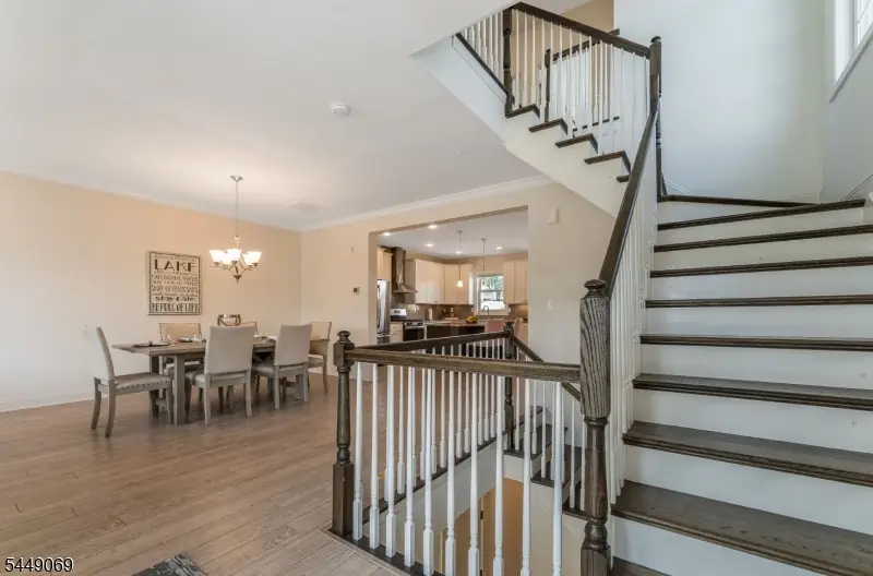 Open dining area with a farmhouse table, a LAKE sign, and hardwood floors, opening past the staircase to the white kitchen at the Lakepointe townhome