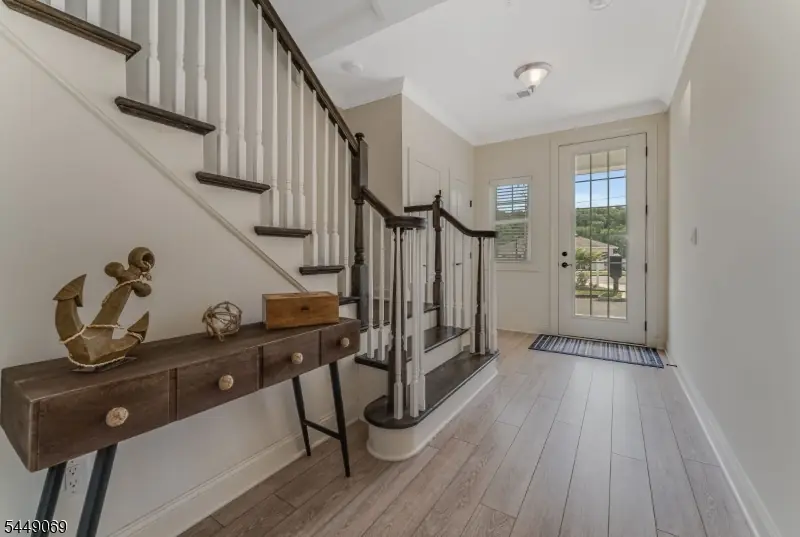 Entry foyer with light wood-look flooring, a glass-panel front door, a hardwood staircase with white balusters, and a driftwood console at 468 River Styx Road