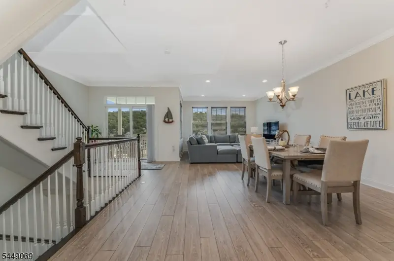 Open-concept living and dining level with hardwood floors, crown molding, a gray sectional by the balcony sliders, and a dining table beneath a chandelier at 468 River Styx Road