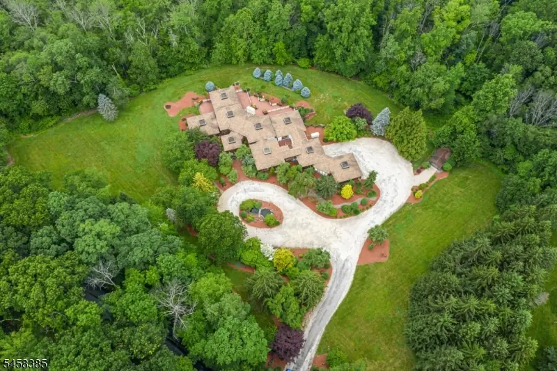 Aerial view of 51 Hoagland Road, Blairstown NJ — a sprawling cedar-shingled custom estate set on eight private wooded acres, ringed by manicured gardens and a circular drive. Listing courtesy of Robin Dora, Prominent Properties Sotheby's International Realty.